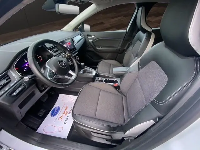 Vue intérieure côté conducteur du Renault Captur blanc nacré 2021, sièges tissu gris et noir, tableau de bord moderne avec écran tactile.