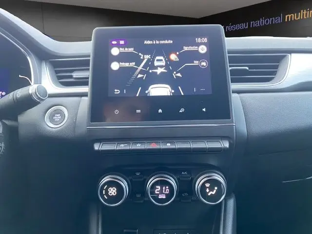 Vue frontale de l’écran tactile et de la console centrale du Renault Captur blanc nacré 2021 avec affichage des aides à la conduite.