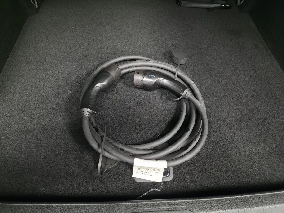 Câble de recharge électrique noir enroulé dans le coffre d'une Peugeot 408 E--210 Allure 2024.