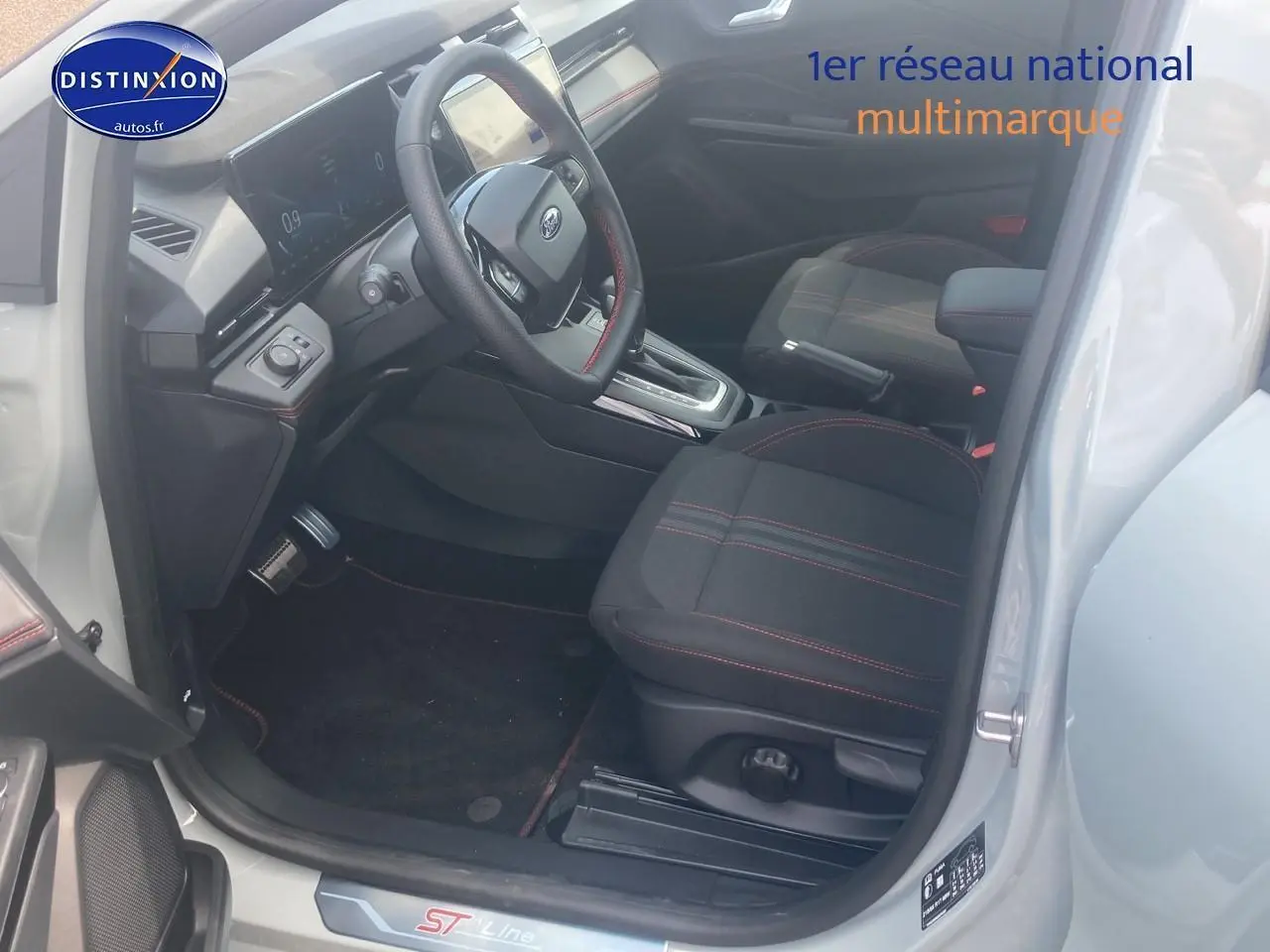 Intérieur avant droit du Ford Puma gris cactus 2025, sièges tissu noir avec surpiqûres rouges et volant multifonction.