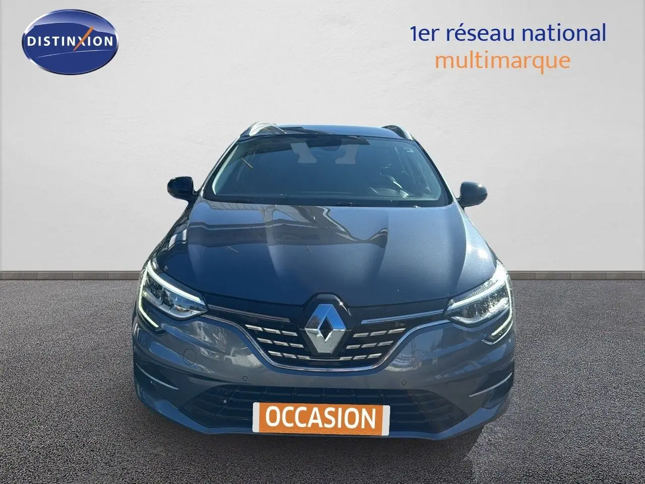 Vue frontale d'une Renault Mégane Break gris titanium métal avec calandre et phares LED allumés.