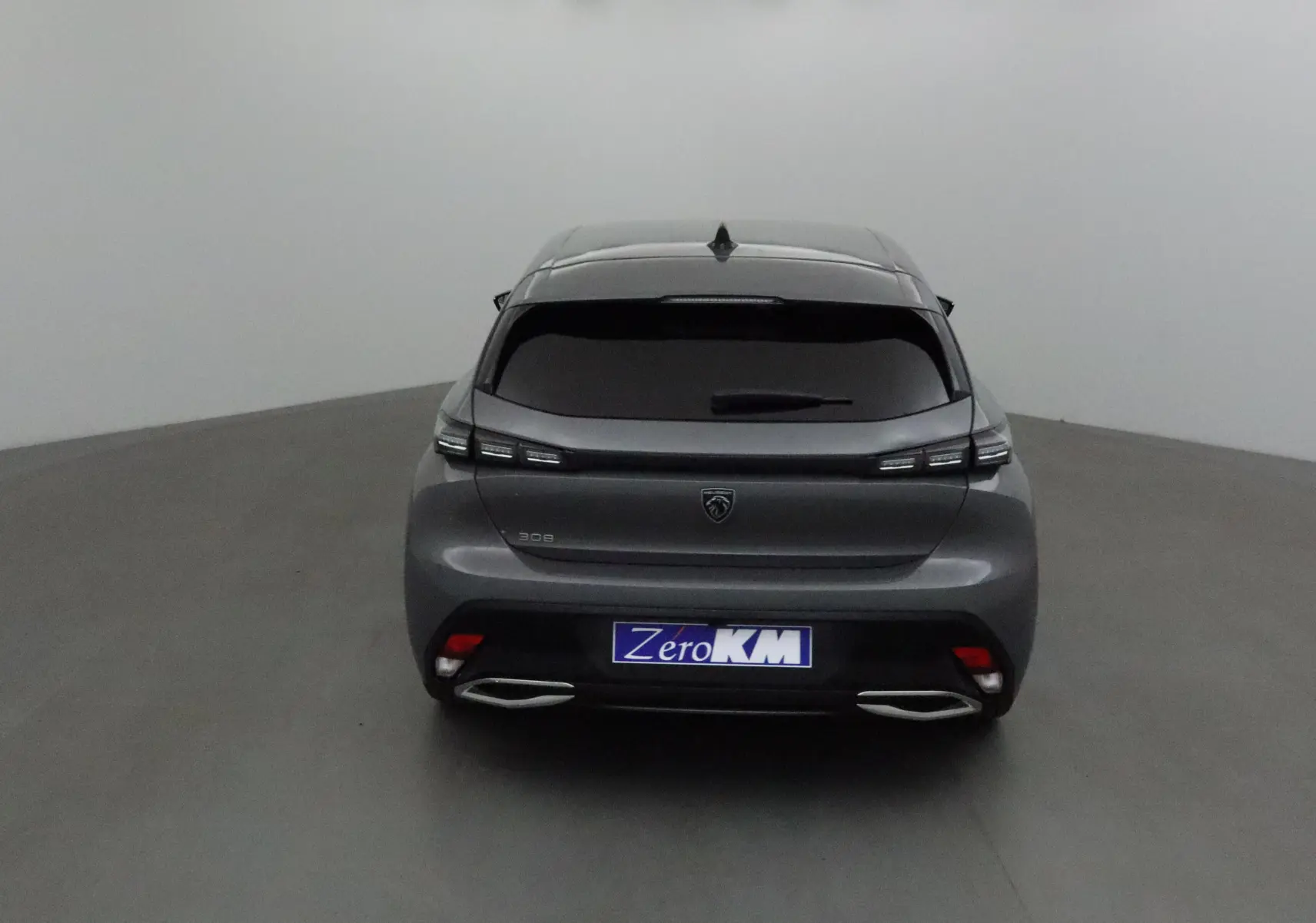 Vue arrière d'une Peugeot 308 gris Sellenium avec feux LED et double sortie d'échappement chromée dans un studio.