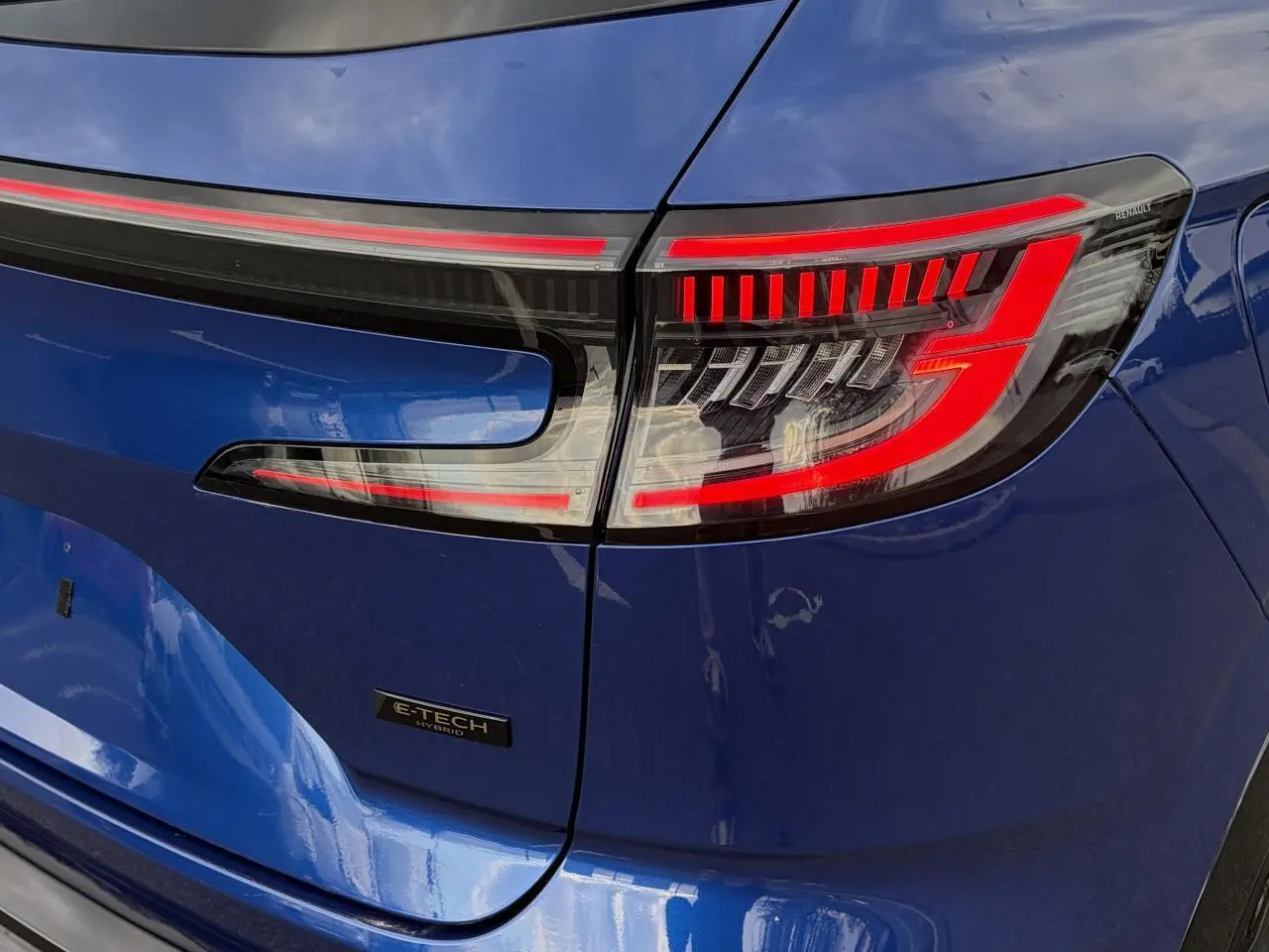 Gros plan sur le feu arrière droit rouge et noir du Renault Austral Bleu Iron avec logo E-Tech Hybrid sur la malle.
