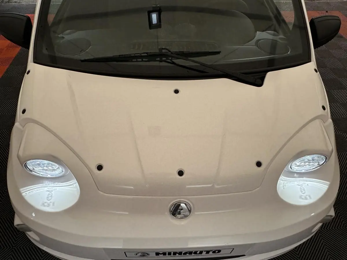 Vue plongeante avant d'une Aixam Minauto E Access blanche, mettant en valeur ses phares ronds et son capot épuré.