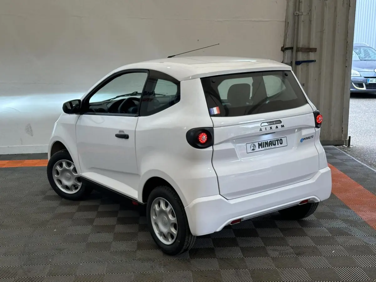 Vue 3/4 arrière droite d'une AIXAM MINAUTO E ACCESS blanche, petite citadine électrique avec feux ronds et caméra côté conducteur.