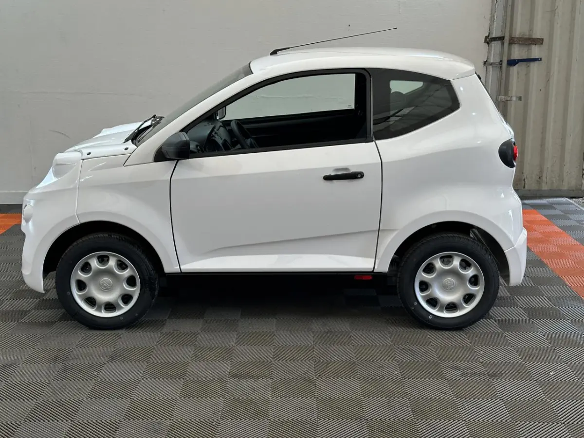 Vue de profil côté gauche de l'AIXAM MINAUTO E ACCESS 2026 blanche, compacte avec rétroviseur caméra côté conducteur.