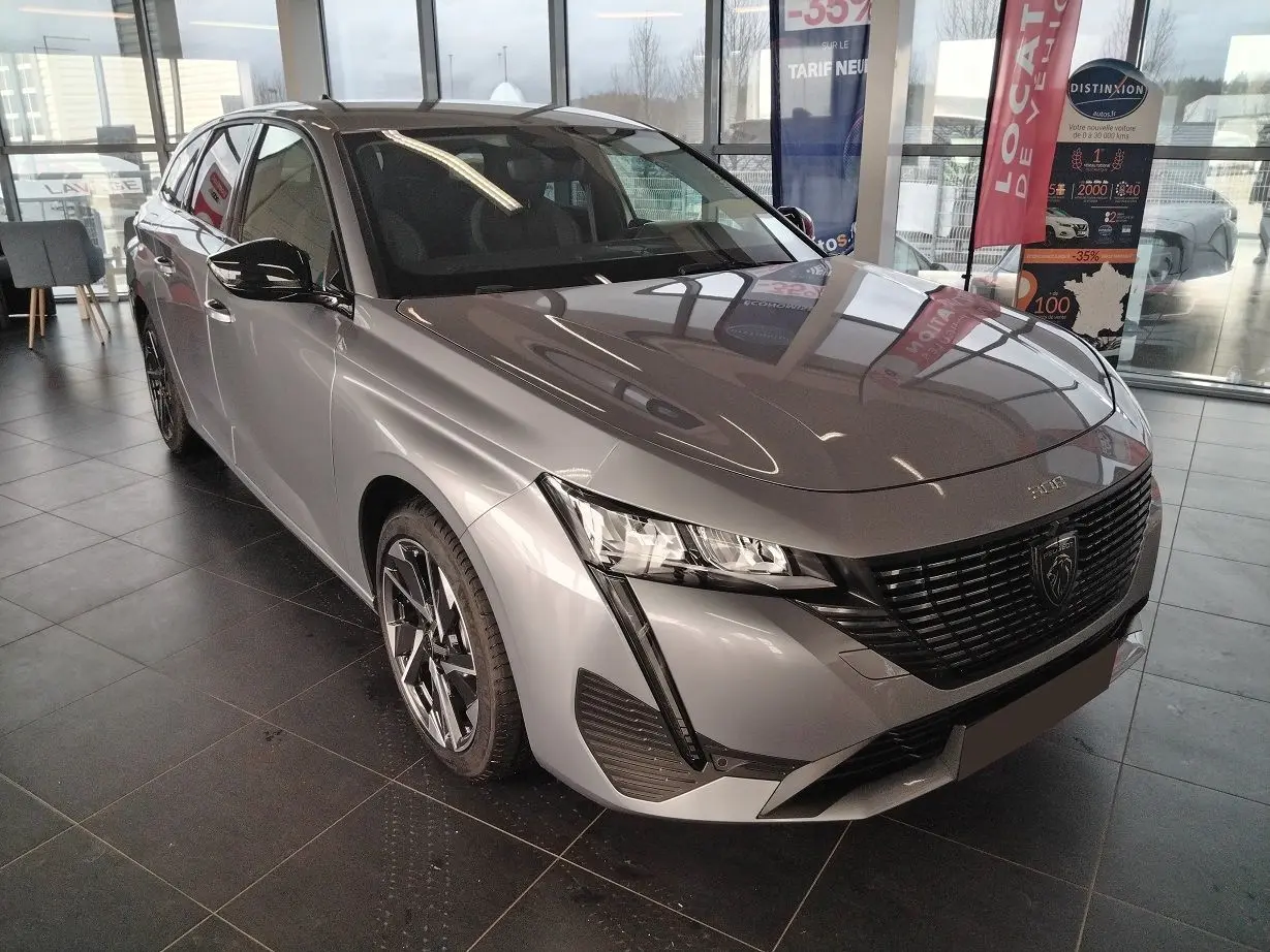 Peugeot 308 SW Hybrid gris Artense vue 3/4 avant gauche en showroom avec jantes bi-ton et calandre noire.
