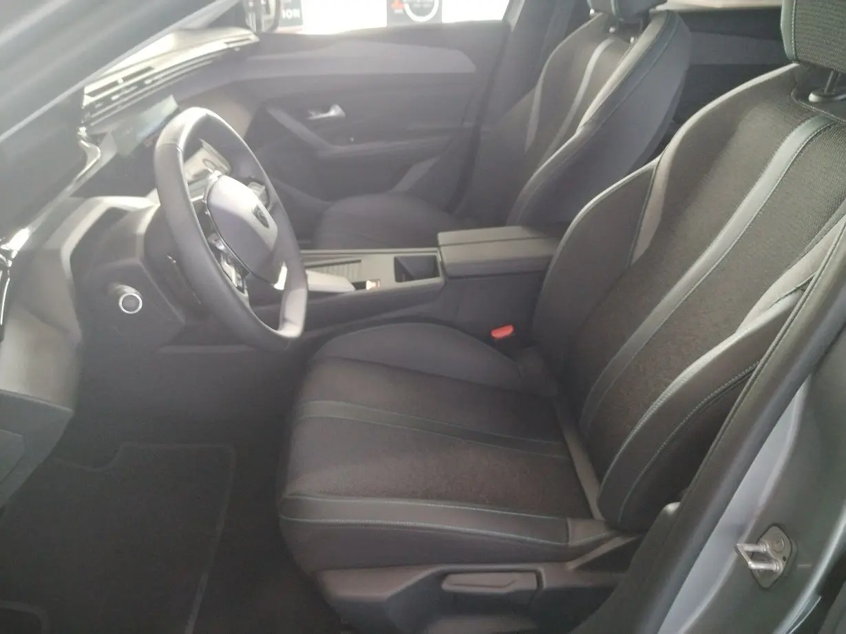 Vue intérieure côté conducteur de la Peugeot 308 SW Hybrid 145 e-DCS6 Allure 2025, sièges noirs et tableau de bord moderne.