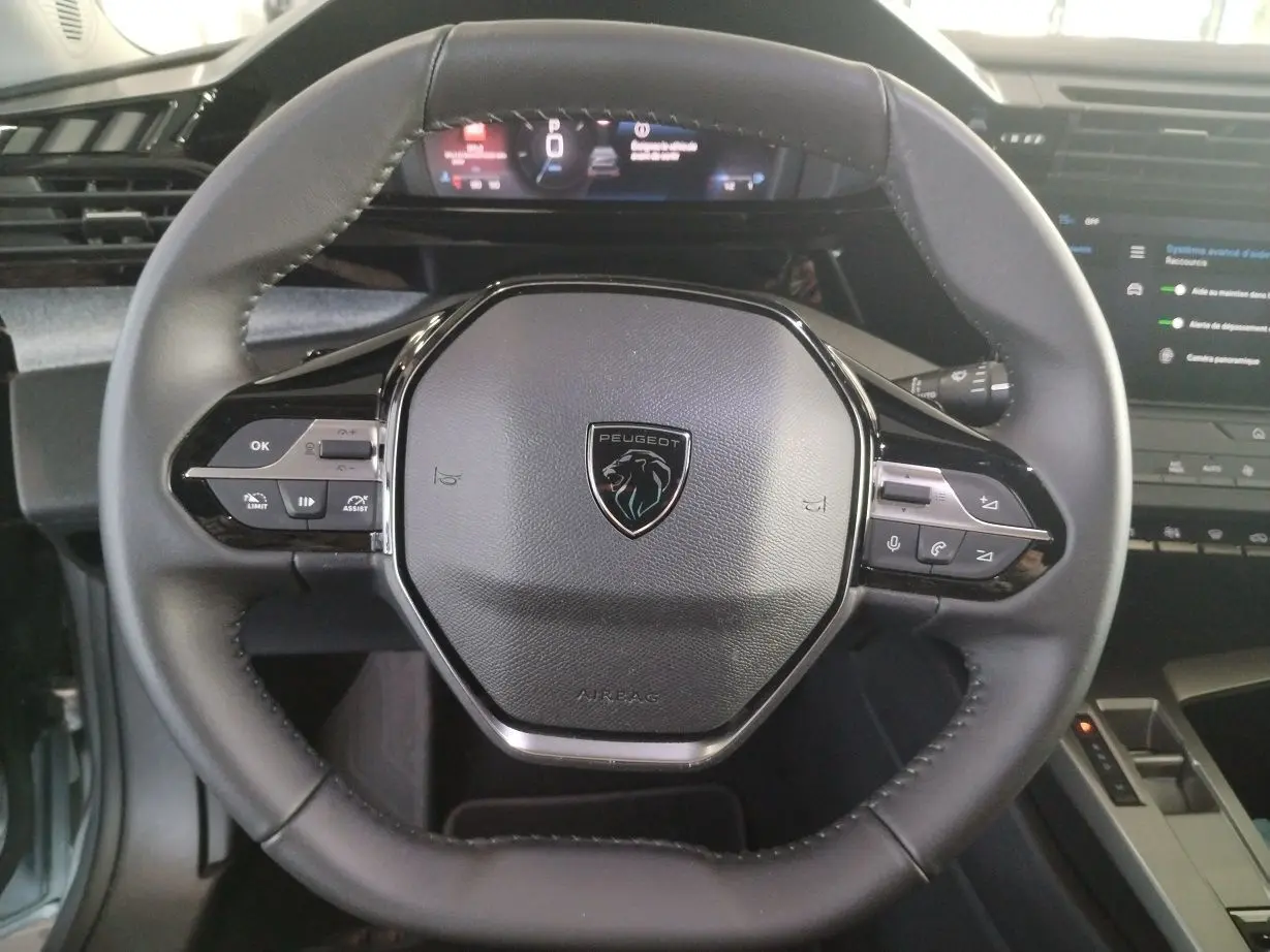 Gros plan sur le volant cuir noir du Peugeot 308 SW Hybrid 145 e-DCS6 Allure avec logo lion et commandes intégrées.