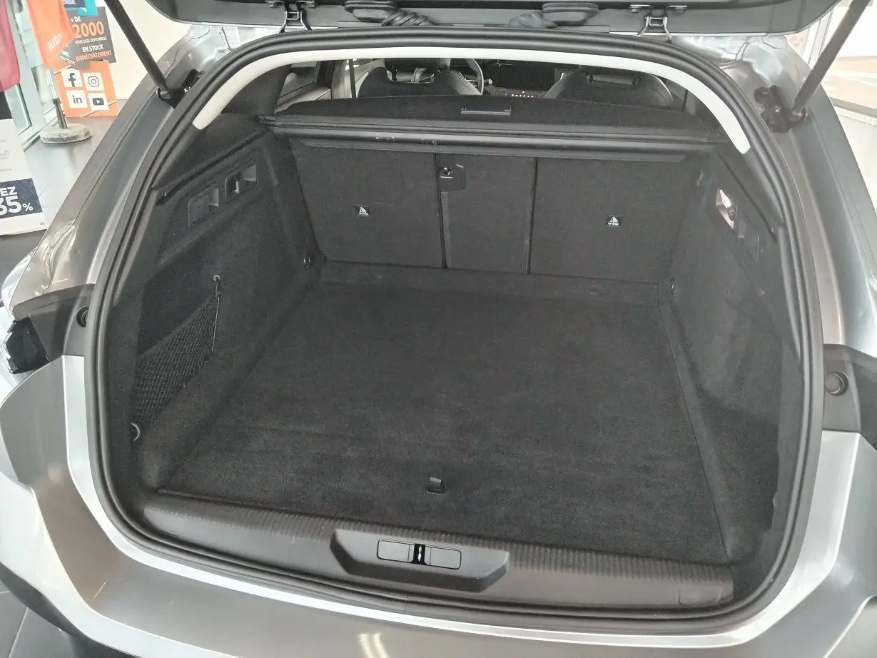 Coffre ouvert vu de l'arrière d'une Peugeot 308 SW Hybrid 145 gris Artense, montrant un espace de chargement spacieux et propre.