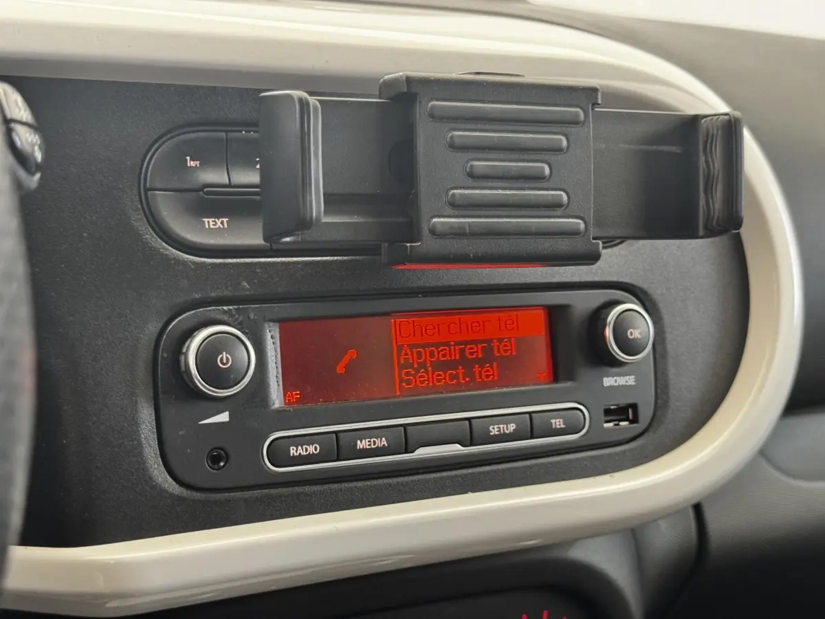 Console centrale avec écran radio rouge et support téléphone dans une Renault Twingo gris foncé, vue intérieure rapprochée.