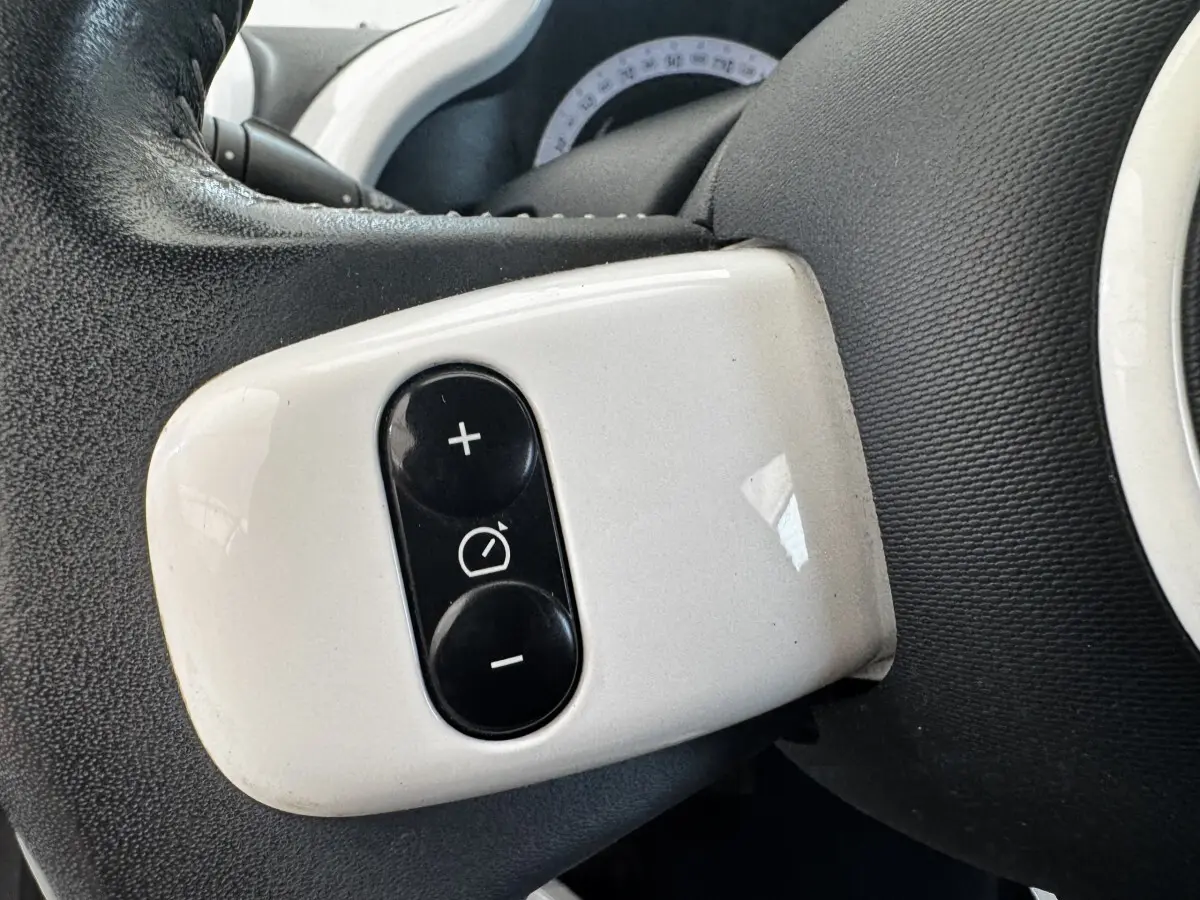 Gros plan sur les commandes blanches du régulateur de vitesse sur le volant cuir noir de la Renault Twingo Intense Energy 2016.