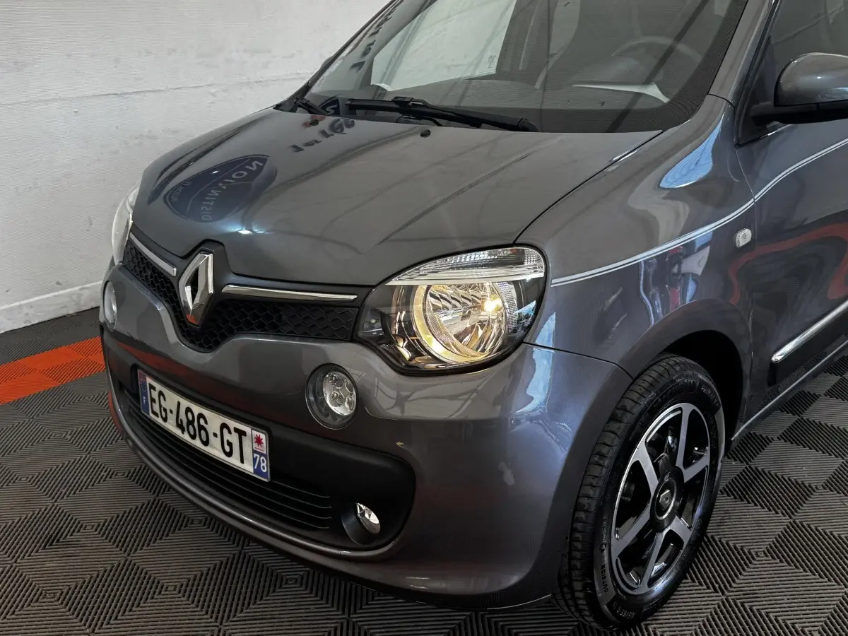 Vue 3/4 avant droit d'une Renault Twingo Intense Energy TCe 90 gris foncé avec phares allumés et jantes noires.