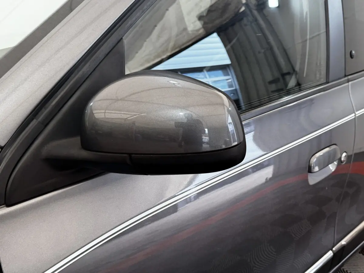 Gros plan sur le rétroviseur côté conducteur d'une Renault Twingo gris foncé avec bande blanche décorative sur la porte.