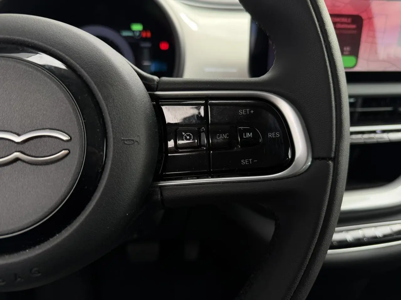 Gros plan sur le volant noir Soft-Touch de la Fiat 500 électrique, avec commandes de régulateur de vitesse visibles.