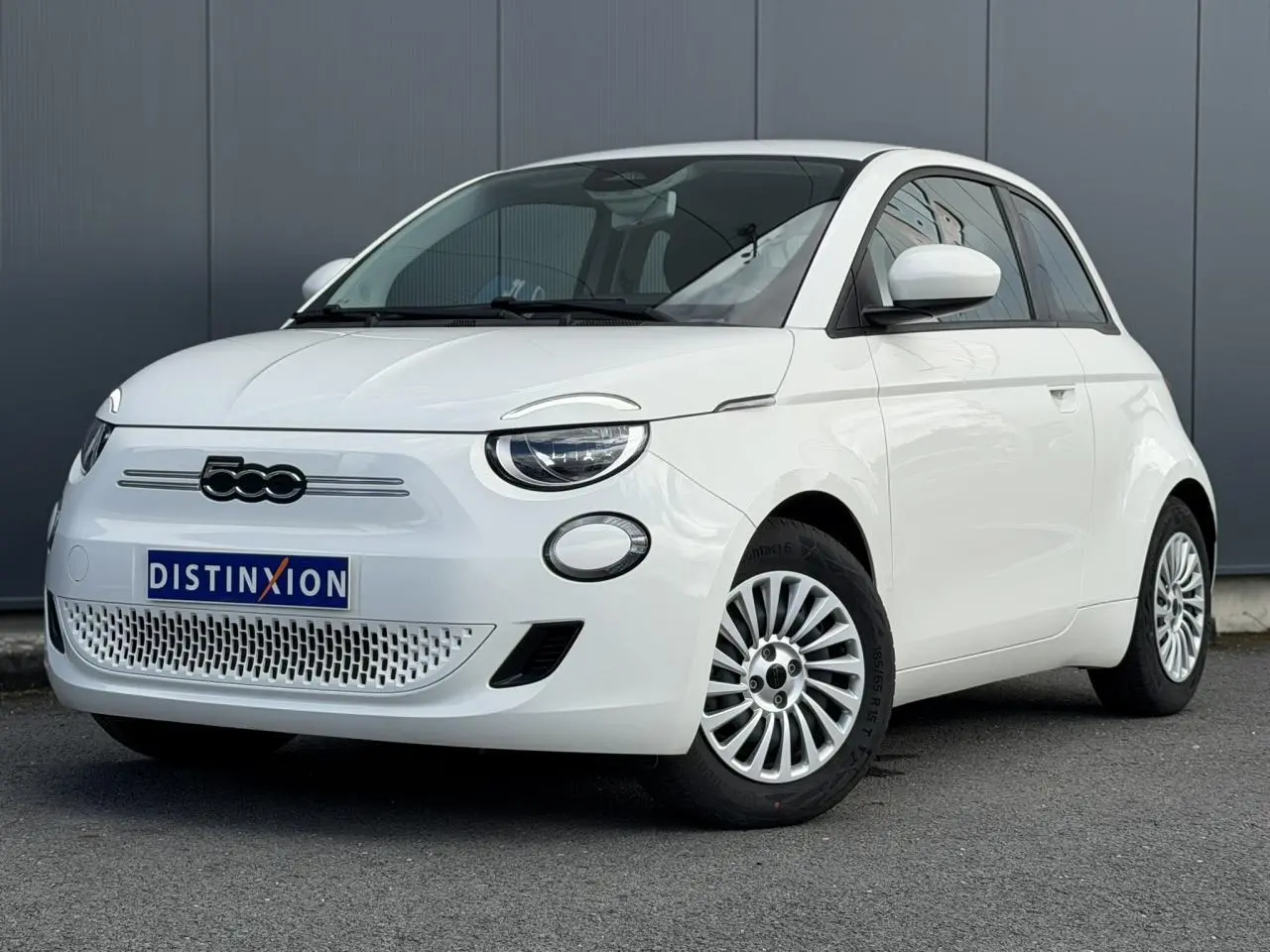 Vue 3/4 avant droite d'une FIAT 500 électrique blanche Arctic avec jantes multibranches et logo noir sur calandre.