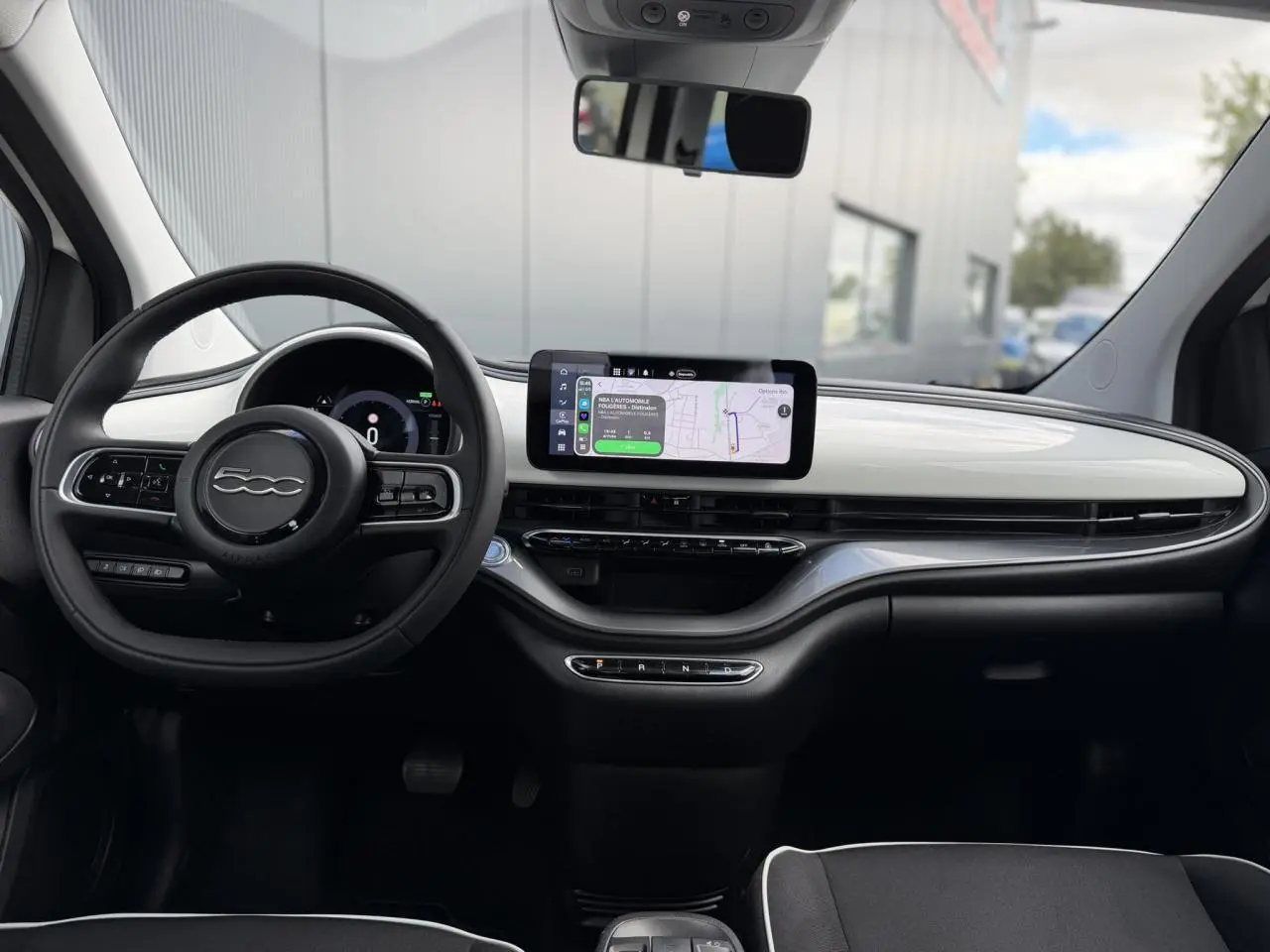 Intérieur du Fiat 500 électrique 2024 vu de face, tableau de bord blanc Artic avec écran tactile central et volant noir Soft-Touch.