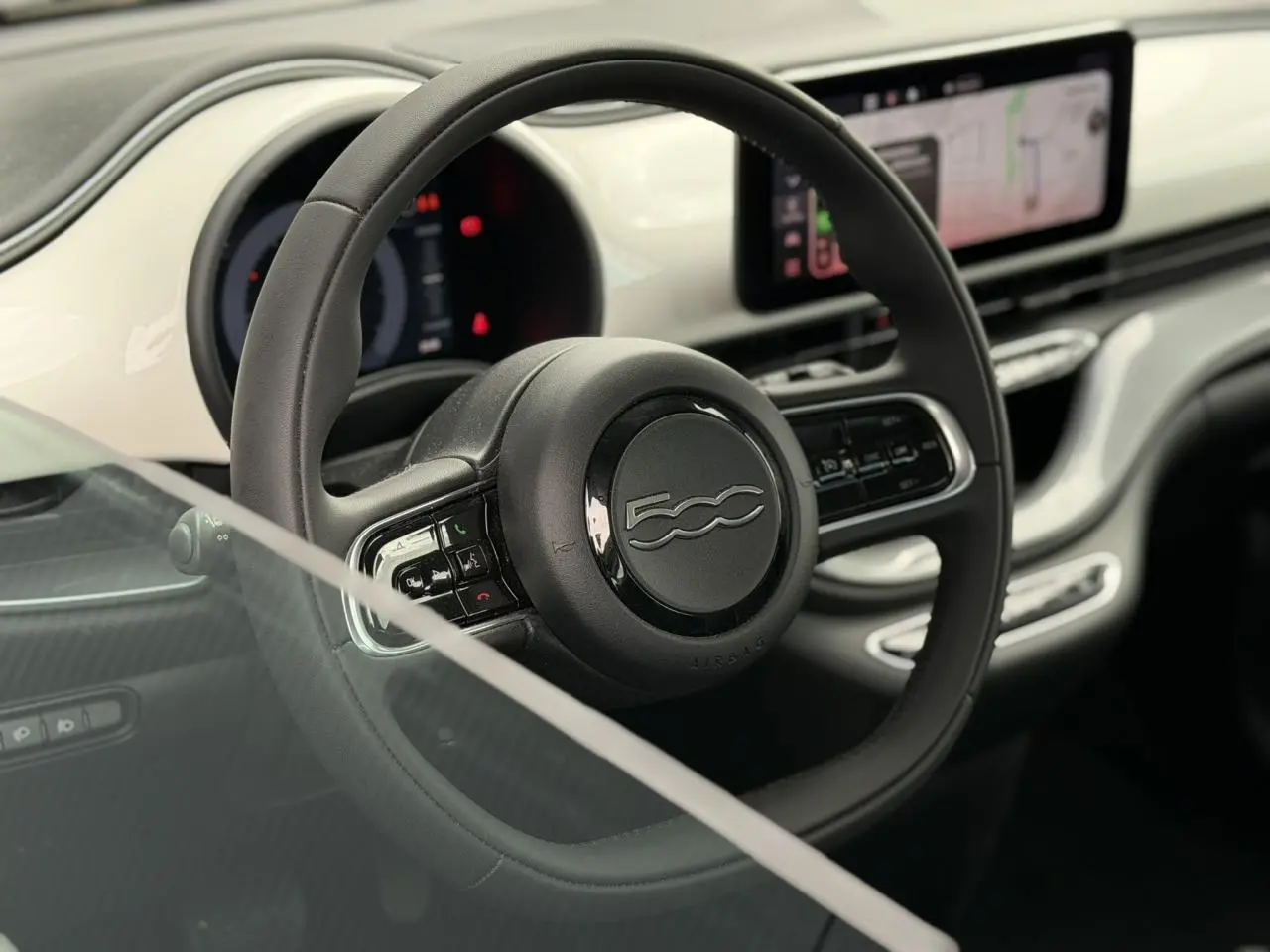 Intérieur de la Fiat 500 électrique 2024, vue centrée sur le volant noir Soft-Touch et planche de bord blanche Artic.