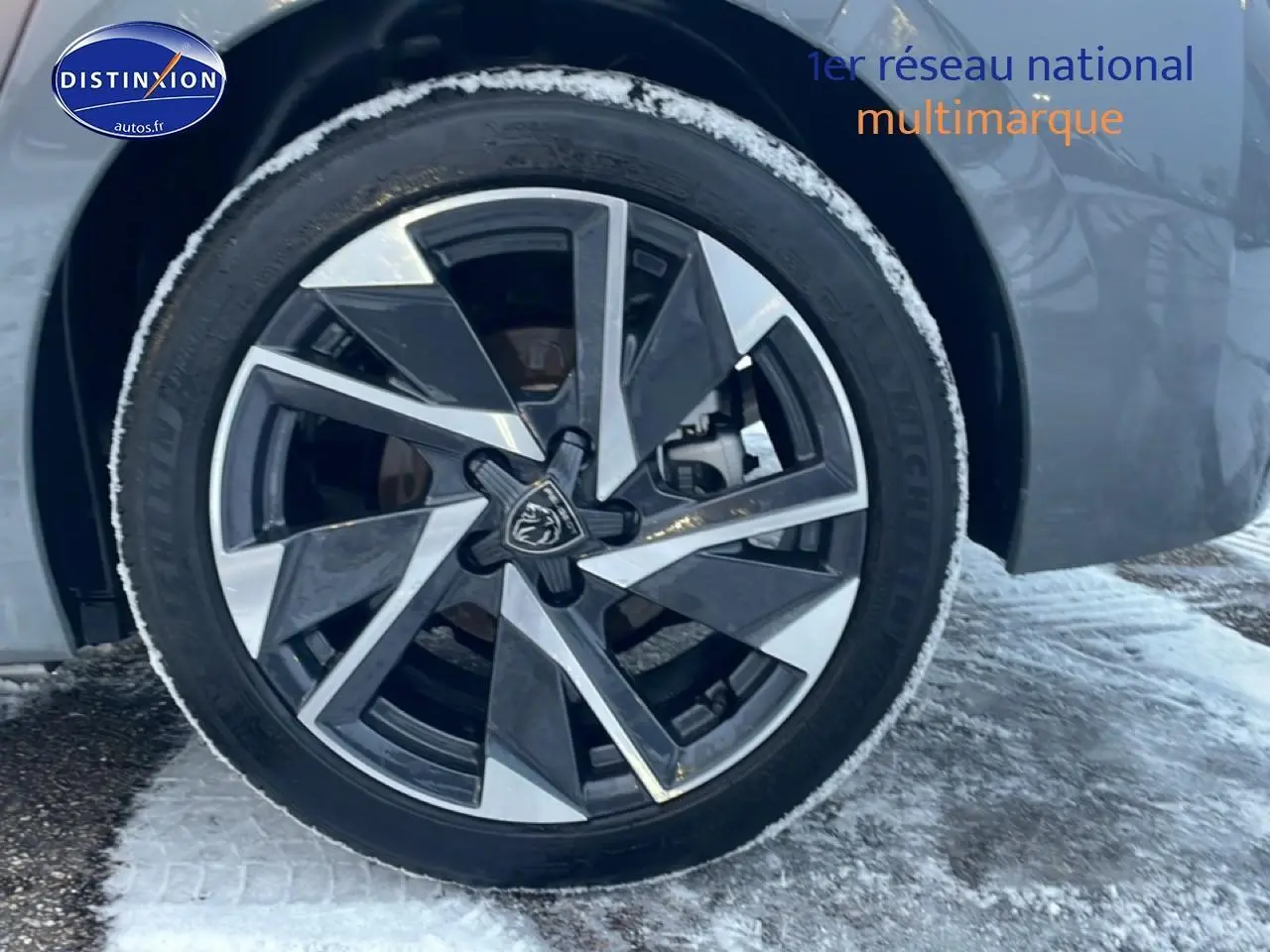 Gros plan sur la jante alu avant droite d’une Peugeot 308 gris sélénite avec neige au sol.