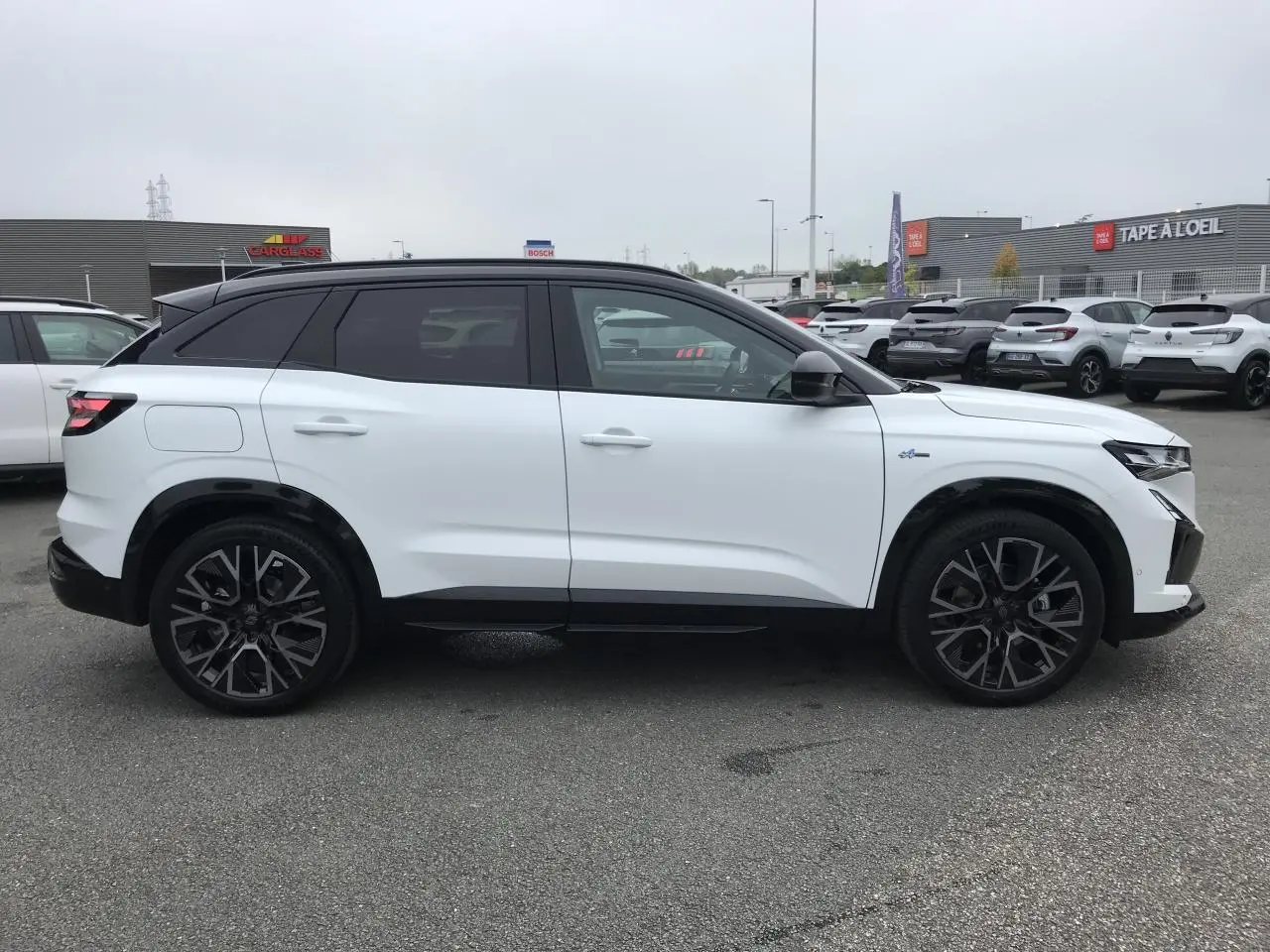 Vue de profil côté gauche d'un Renault Austral blanc bi-ton avec jantes noires et toit noir satin.