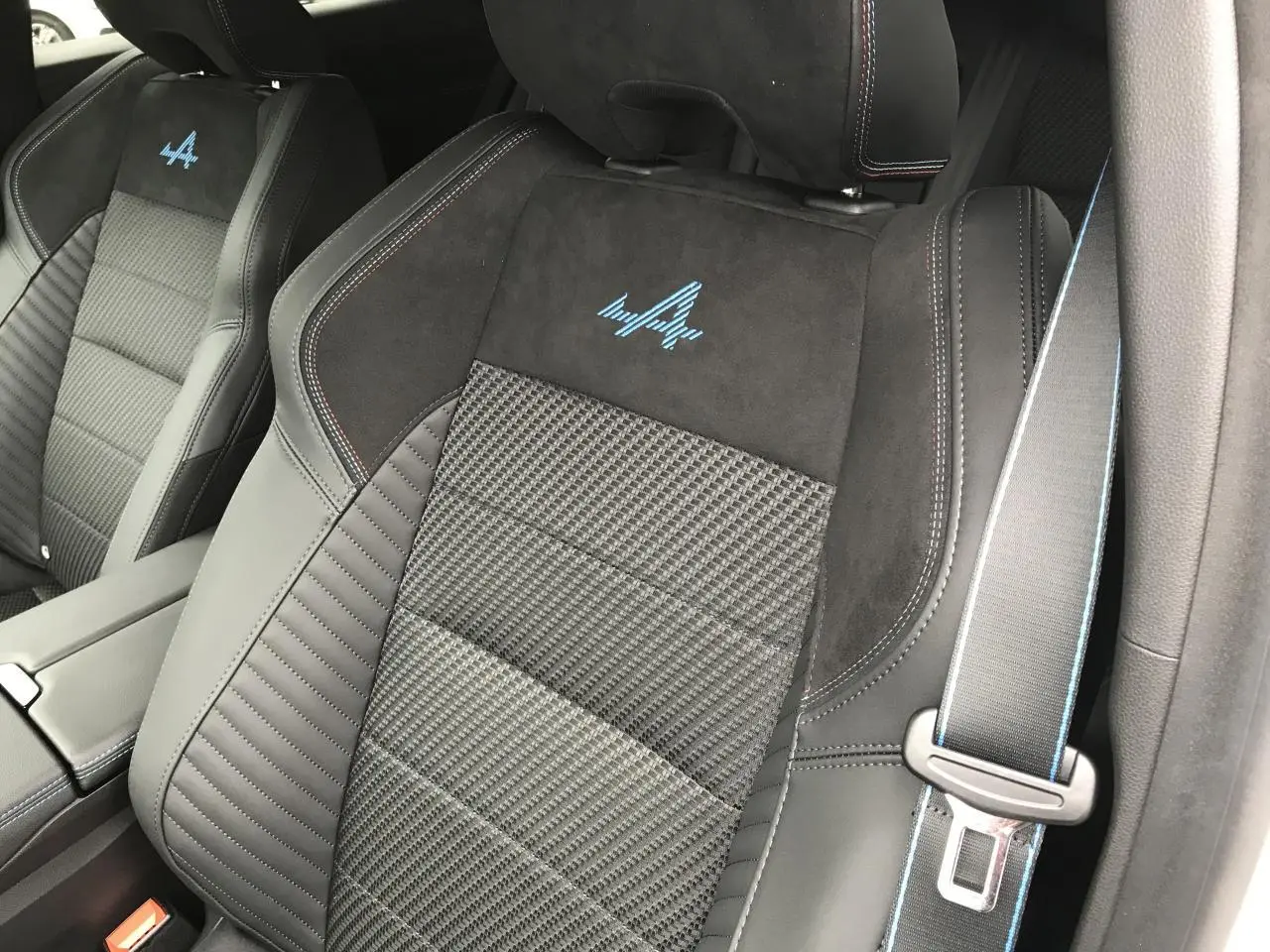 Gros plan sur le siège avant droit en tissu carbone et alcantara noir avec surpiqûres et logo Alpine bleu visible.