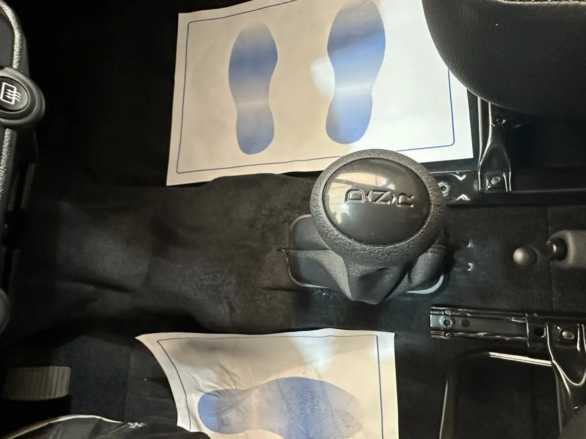 Vue intérieure centrée sur le levier de vitesse automatique noir avec logo Aixam, entouré de tapis de sol noirs.