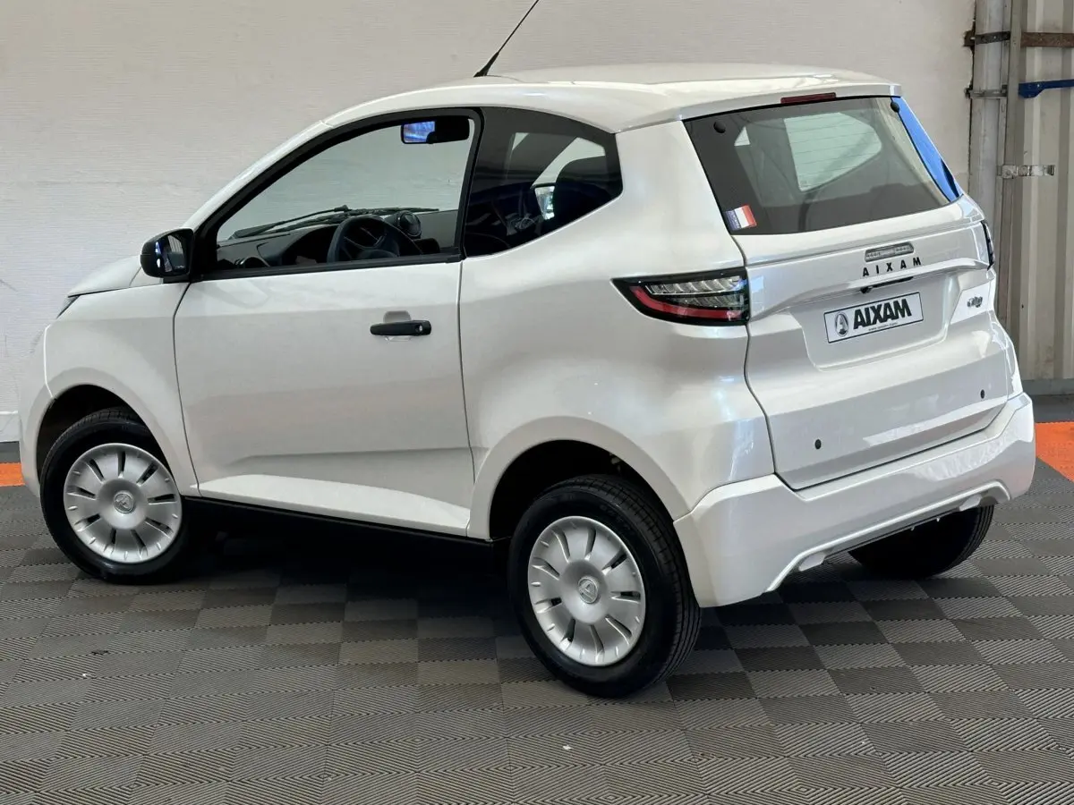 Vue 3/4 arrière côté gauche d'une Aixam Ambition E City Pack blanche 2026 avec rétroviseur caméra côté conducteur.