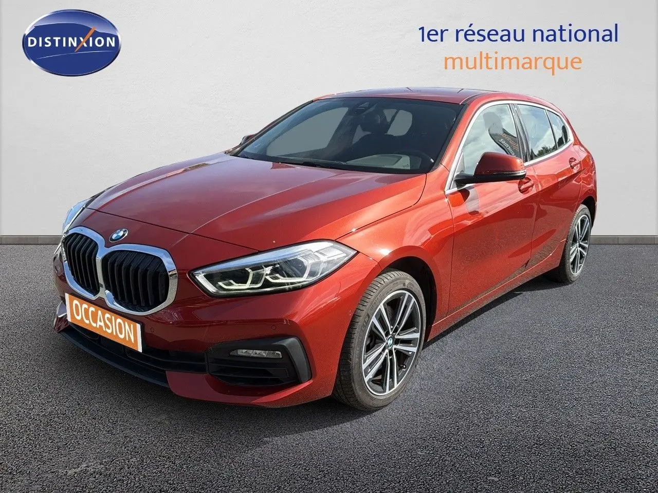 BMW Série 1 116i Business orange Sunset vue 3/4 avant droit, avec calandre imposante et jantes alliage bicolores.