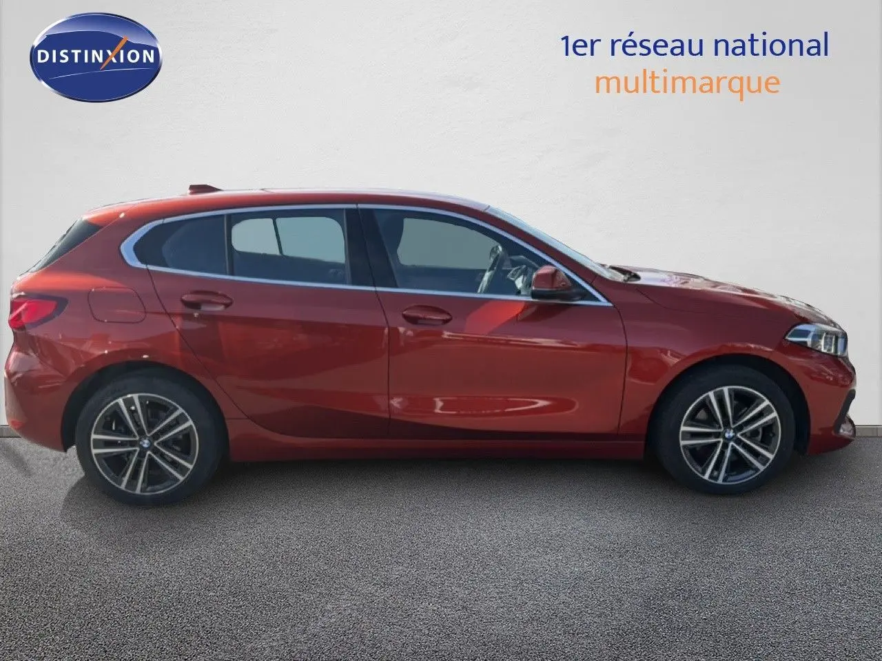 Profil latéral droit d'une BMW Série 1 116i Business 2022 en orange Sunset métallisé, avec jantes alliage et vitres teintées.