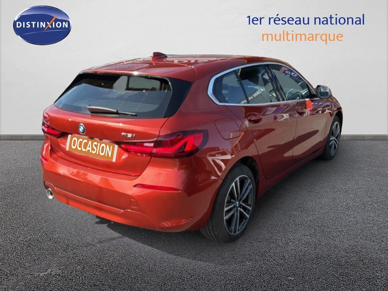 Vue 3/4 arrière droite d'une BMW Série 1 116i Business en orange Sunset métallisé avec jantes alliage et feux LED.