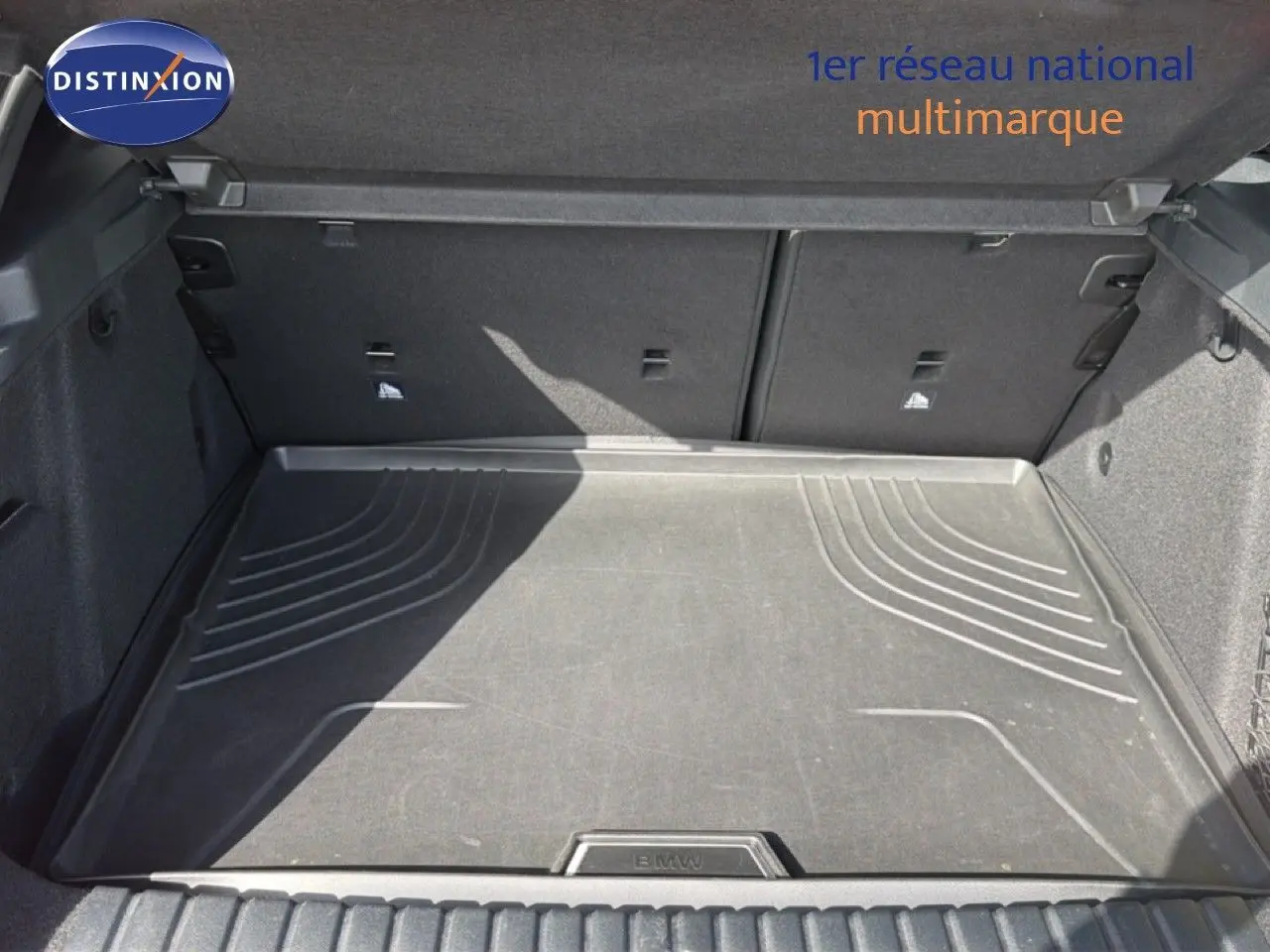 Coffre ouvert vu de face, tapis de sol noir avec logo BMW, intérieur spacieux et revêtement gris foncé.