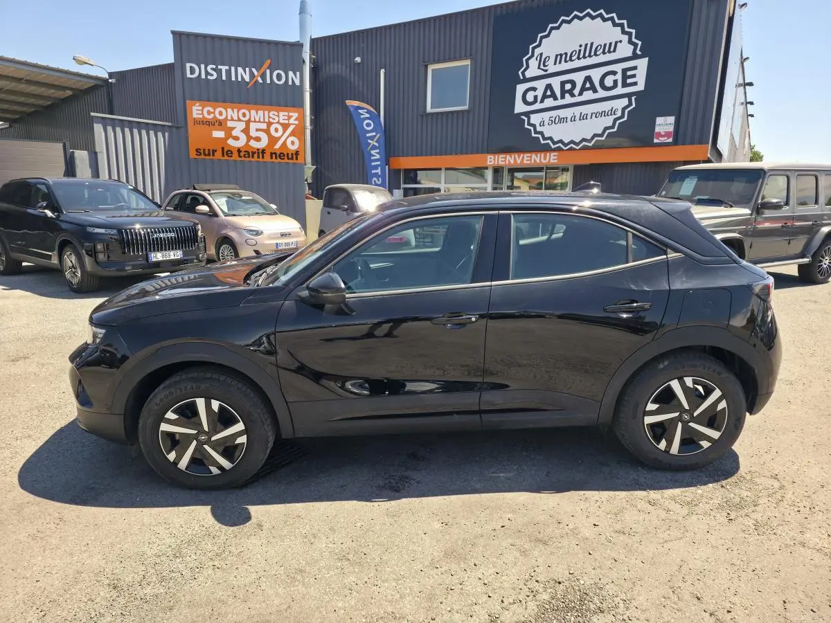 Opel Mokka noir vue de profil côté gauche, avec jantes bicolores et toit couleur carrosserie, stationné devant un garage.