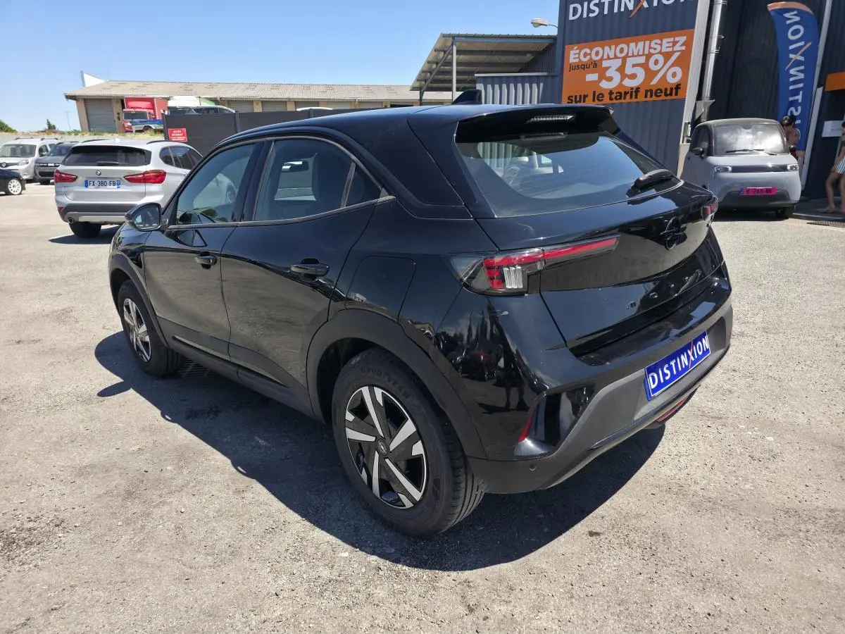 Opel Mokka noir vue 3/4 arrière droit, avec jantes bicolores et toit couleur carrosserie sur parking extérieur.