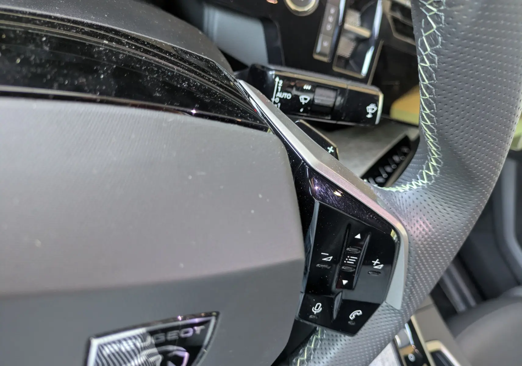 Gros plan sur le volant perforé gris avec surpiqûres vert clair du Peugeot 3008 Hybrid 145 GT, boutons multifonctions visibles.