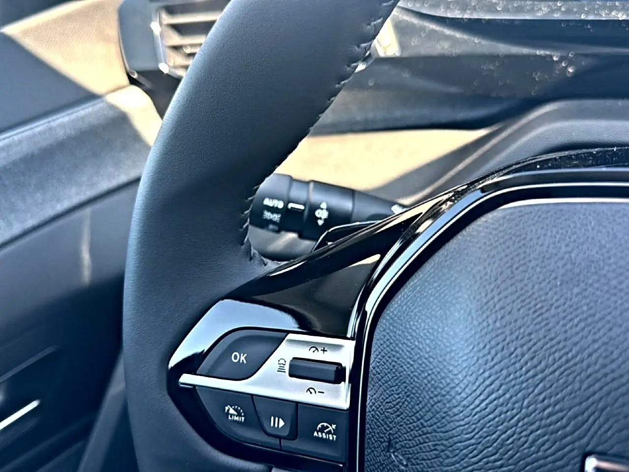 Gros plan sur le volant cuir noir du Peugeot 408 Hybrid 145 allure e-dcs6, avec commandes intégrées côté gauche.