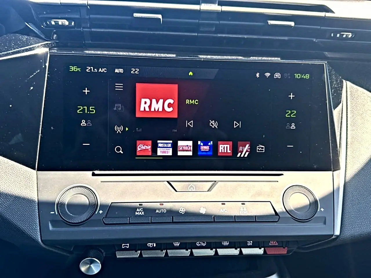Écran tactile central du tableau de bord du Peugeot 408 noir, affichant la radio RMC et commandes climatisation.