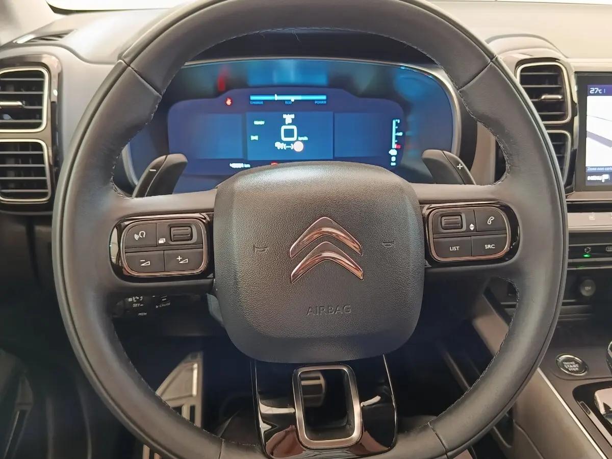 Vue rapprochée du volant cuir multifonctions du Citroën C5 Aircross Hybrid 225 ë-EAT8 avec tableau de bord numérique en arrière-plan.