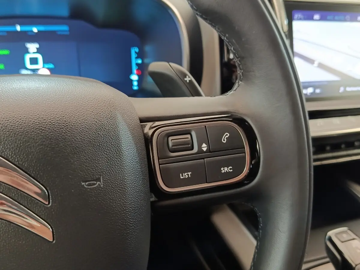 Gros plan sur le volant cuir noir du Citroën C5 Aircross Hybrid 225 ë-EAT8 avec commandes audio et écran tactile de navigation visible.