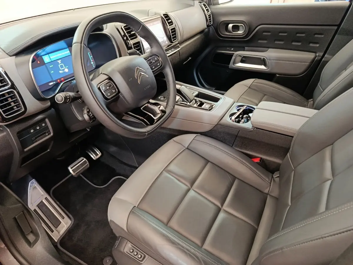 Vue intérieure côté conducteur du Citroën C5 Aircross Hybrid gris foncé, avec volant cuir et tableau de bord digital.