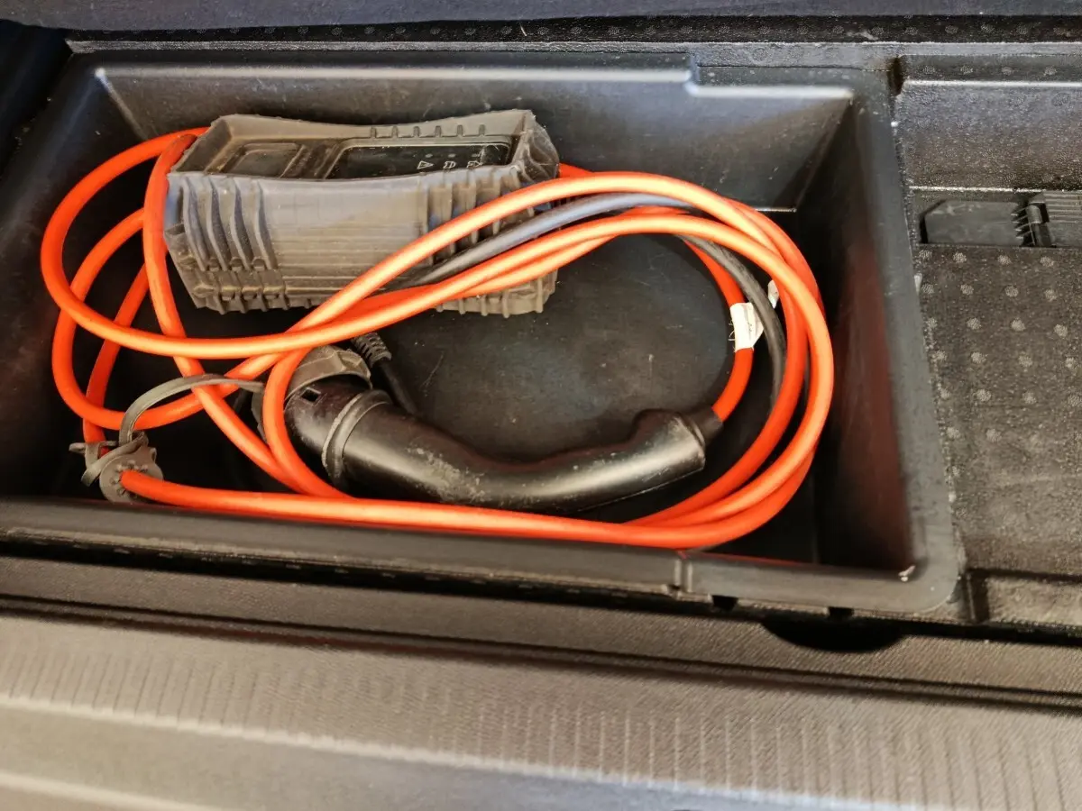 Câble de recharge orange rangé dans le compartiment de coffre du Citroën C5 Aircross Hybrid gris foncé.