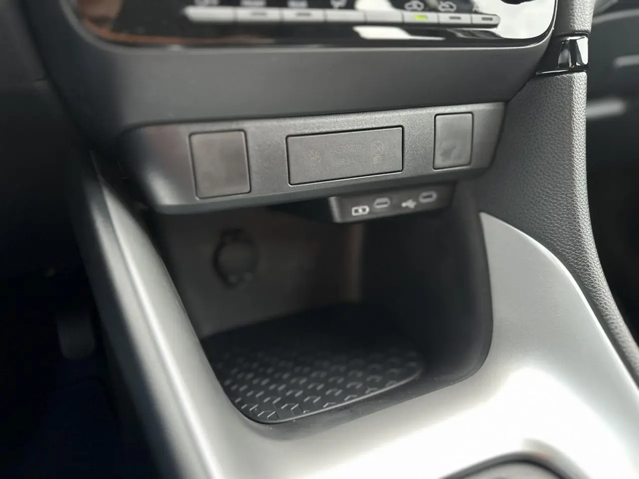 Gros plan sur la console centrale noire et grise de la Toyota Yaris 2025 Hybride avec ports USB-C et rangement antidérapant.