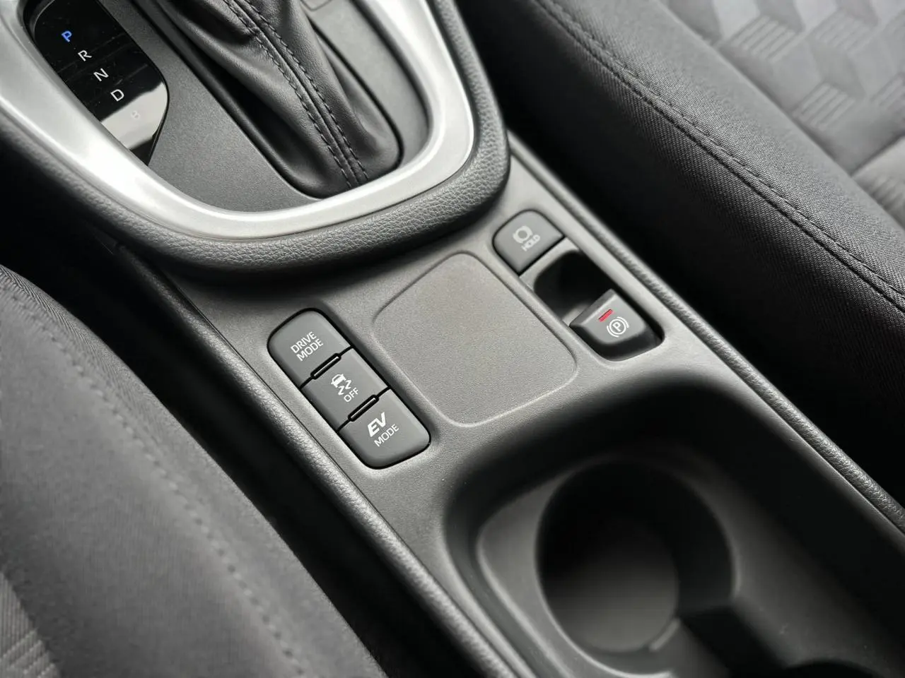 Gros plan sur la console centrale noire de la Toyota Yaris Hybride 2025 avec levier de boîte auto et boutons de modes de conduite.