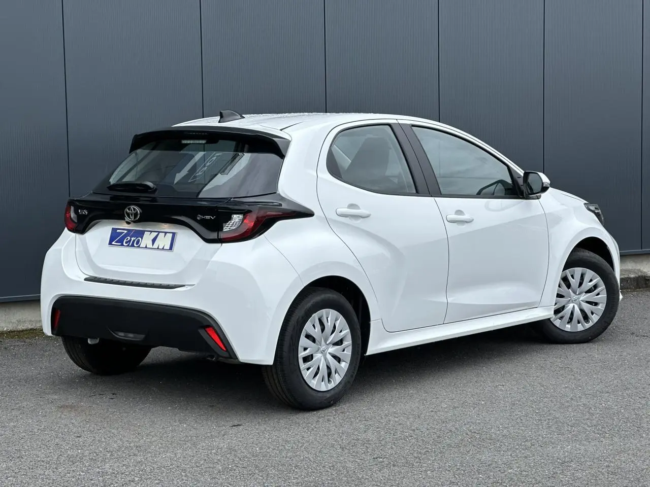 Vue 3/4 arrière droite d'une Toyota Yaris hybride blanche avec toit noir et jantes acier à enjoliveurs.