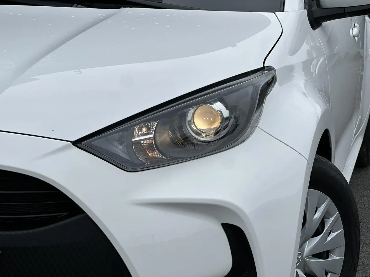 Gros plan sur le phare avant droit d'une Toyota Yaris blanche 2025, soulignant la calandre et la jante acier.