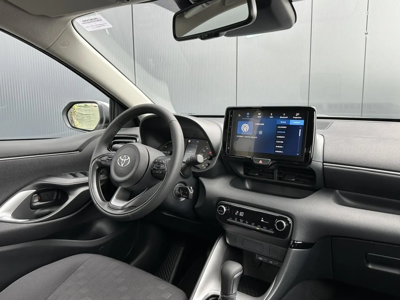Vue intérieure côté conducteur de la Toyota Yaris 2025 hybride, avec tableau de bord noir et écran tactile central allumé.