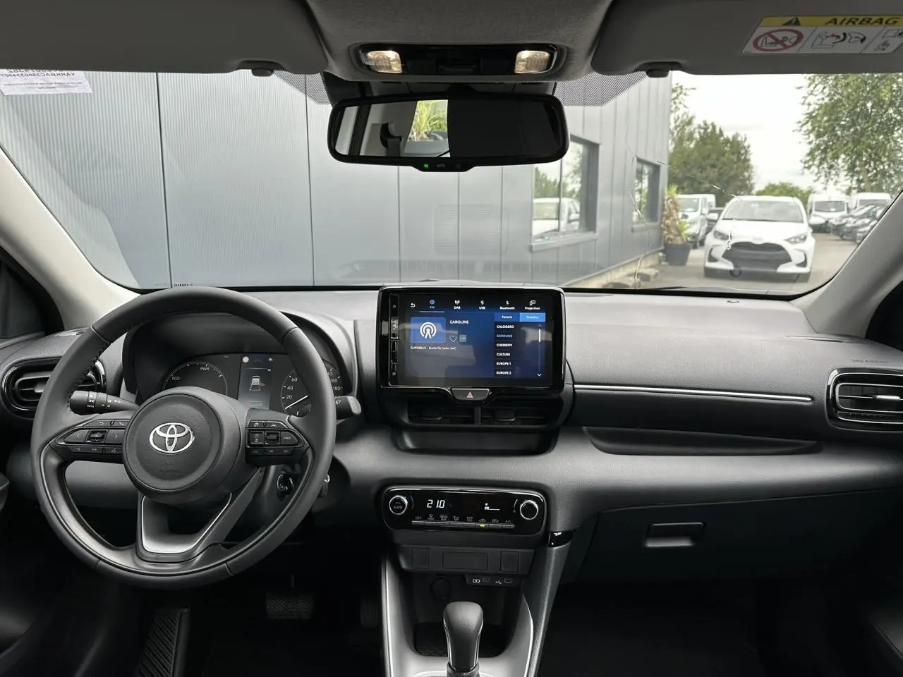 Vue intérieure avant de la Toyota Yaris blanche 2025, tableau de bord moderne avec écran tactile et volant multifonction en cuir.