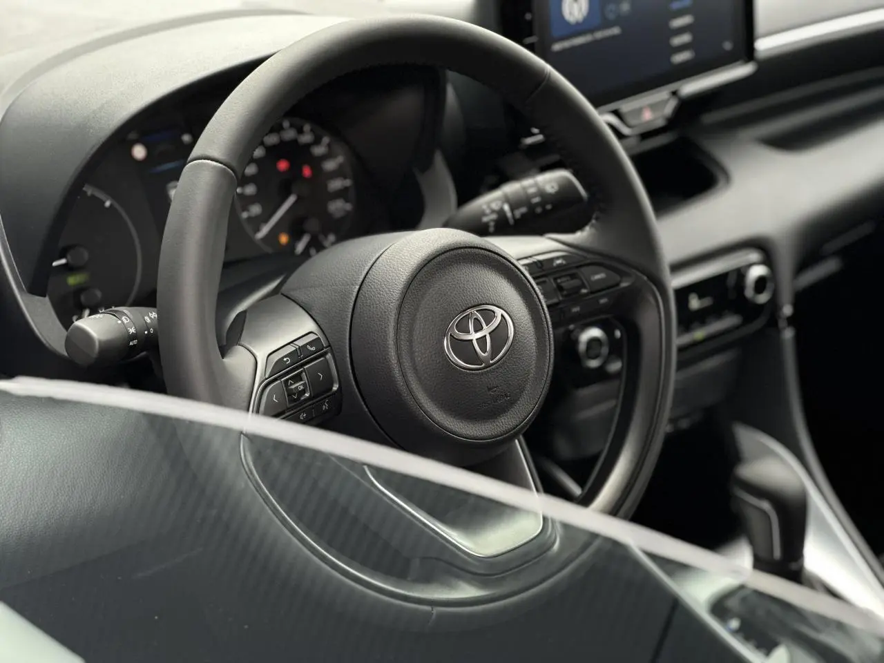 Vue rapprochée du volant en cuir noir de la Toyota Yaris 2025, avec commandes multifonctions et tableau de bord visible.