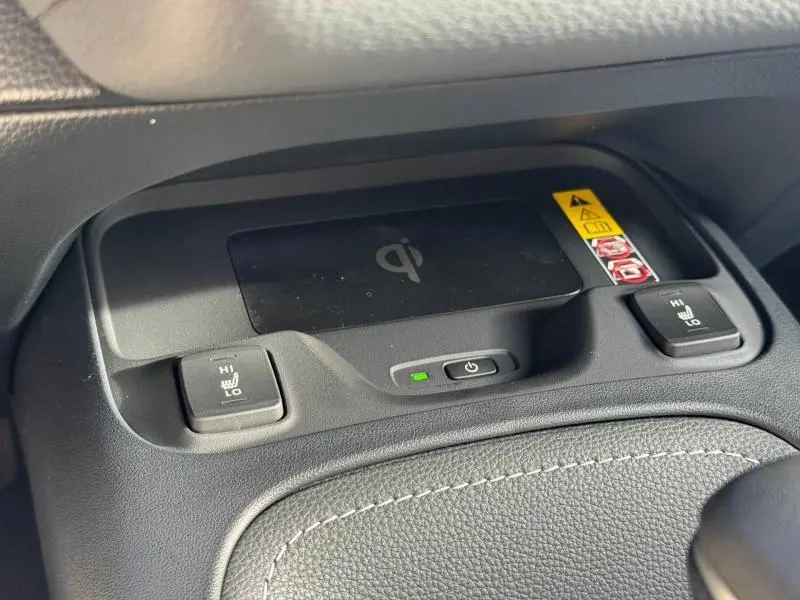 Vue rapprochée du chargeur à induction noir et des commandes de sièges chauffants sur la console centrale d'une Toyota Corolla noire.