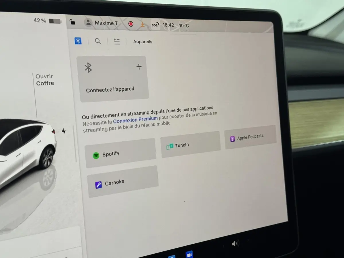 Écran tactile central affichant les options de streaming dans l’habitacle d’un Tesla Model Y blanc, vue intérieure côté passager.