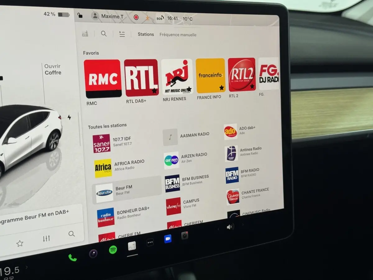 Écran tactile central affichant les stations radio dans l’habitacle d’un Tesla Model Y blanc, vue intérieure côté passager.